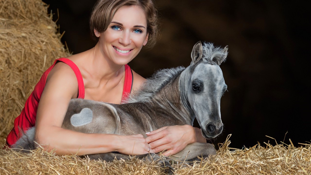 Woman among bales of hay hugging one of the smallest horse breeds in the world