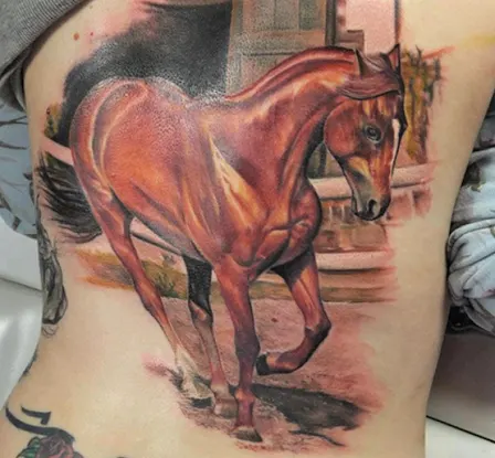 Colorful running horse with a stable in the background tattoo design idea