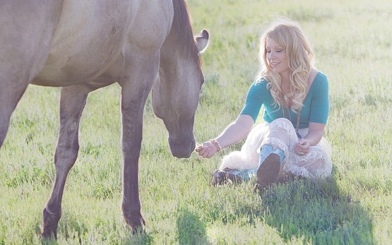 Girl rewarding her horse with a treat in a field