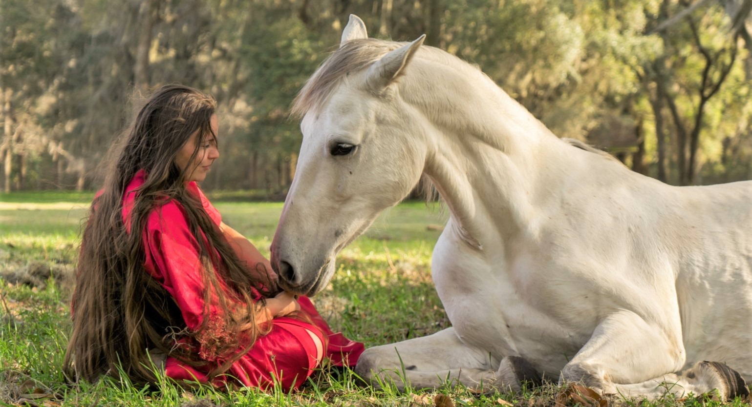 Woman laying down with a white Azteca horse