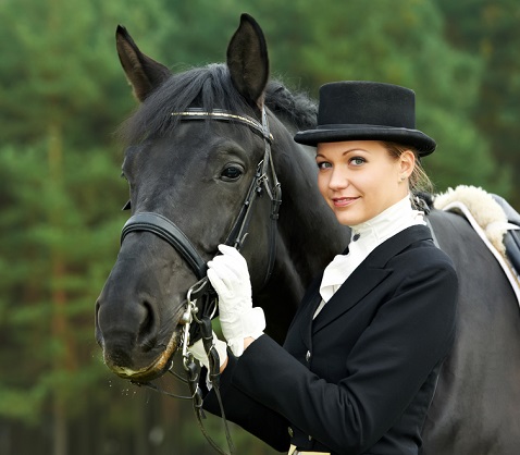 Woman wearing traditional dressage clothing and holding a black horse