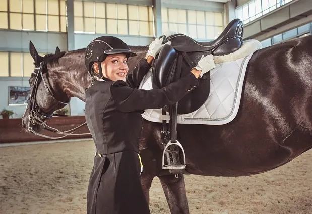 Posh equestrian girl tacking up a horse in a m&eacute;nage