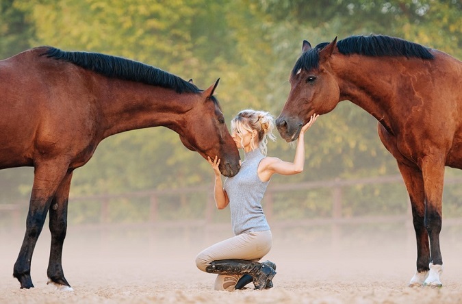 Woman kissing a horse and stroking another at the same time