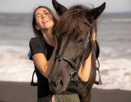 Woman laughing with her horse on the beach