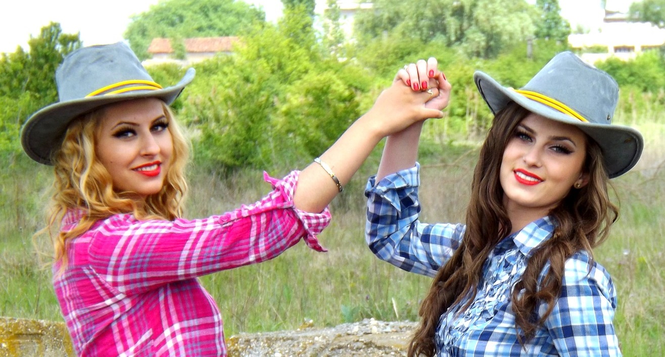 Two women with cowgirl hats on in a field