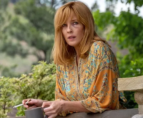 Beth Dutton holding a cigarette and mug of coffee in her hand on the Dutton ranch porch on the Yellowstone TV show