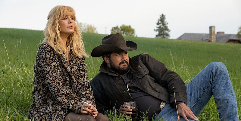 Beth Dutton and Rip Wheeler sitting on grass watching John Dutton's party in Yellowstone season 5