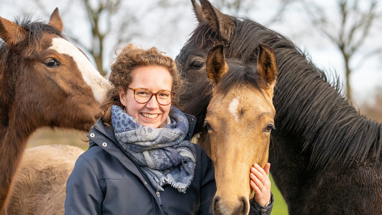 Smiling woman surrounded by three young horses in a field