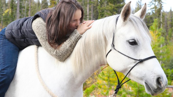 Woman laying on the back of a white horse and facing forward while smiling