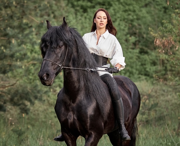 Beautiful long-haired girl riding a black Friesian horse