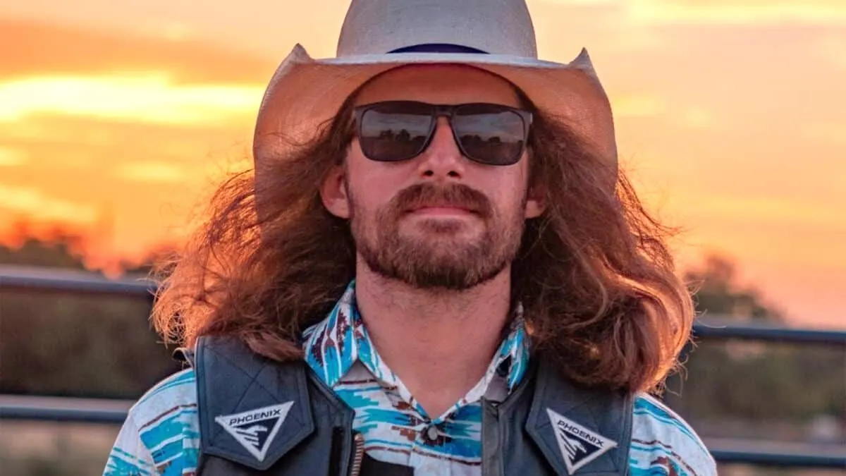 Close up of Dale Brisby wearing sunglasses and a cowboy hat with a sunset background