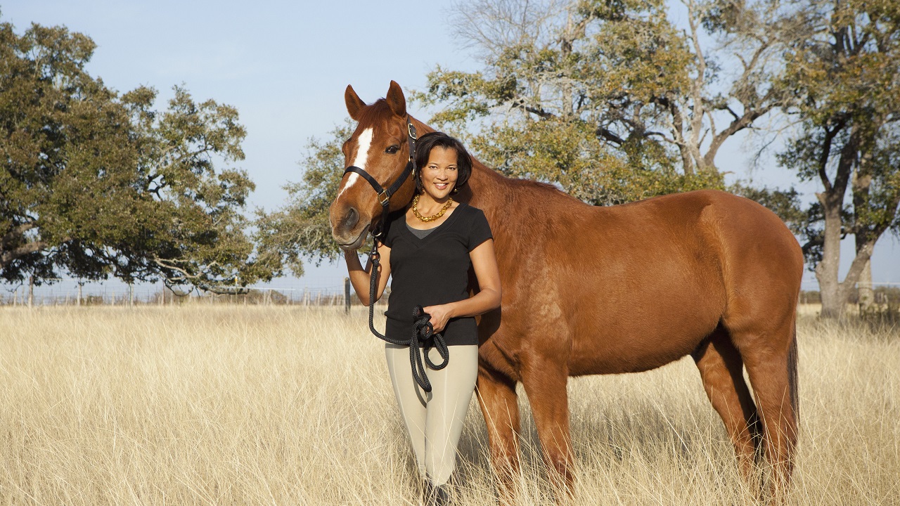 Woman leading a horse on the halter through long dead grassy field