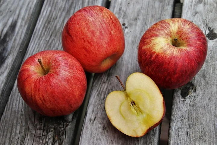 Close up of three whole red apples and one half apple